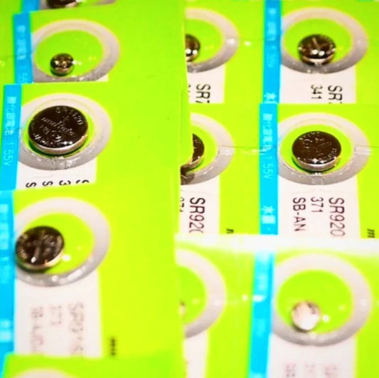 Close-up of packaged watch batteries SR920 371 SB-AN with bright green and blue labels for watch repair