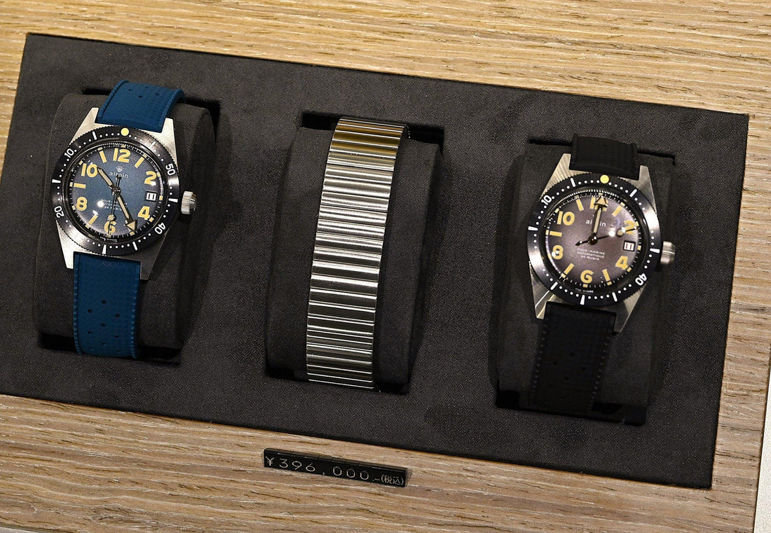 ヴィンテージ風デザインの機械式腕時計2本と金属ベルト、木製ディスプレイ上の高級時計