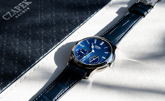 Contévanou Czapek Genève luxury watch with blue guilloché dial and black leather strap on white textured surface