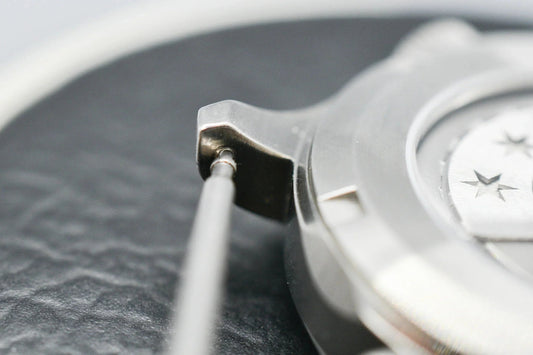 Close-up of mechanical watch case being assembled or repaired with precision tool on a textured surface