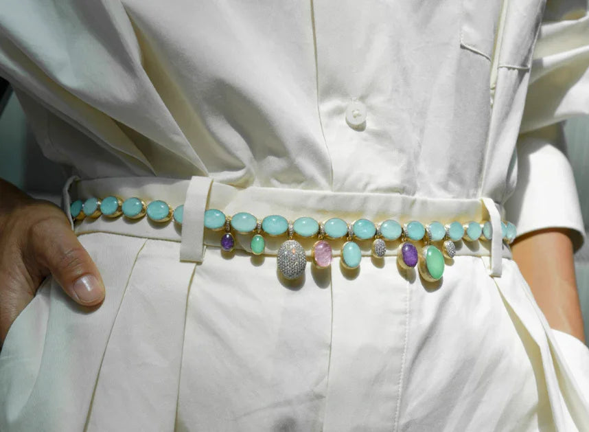 Close-up of a stylish gemstone belt with turquoise, amethyst, and diamond accents worn over white pants and shirt at Contévanou collection