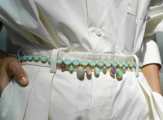 Close-up of a stylish gemstone belt with turquoise, amethyst, and diamond accents worn over white pants and shirt at Contévanou collection