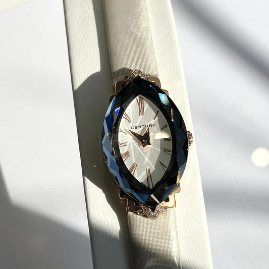 Elegant CENTURY wristwatch with faceted black bezel, gold Roman numerals, and white fabric strap on white surface