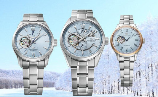 Three automatic Orient Star silver wristwatches with blue dials and visible mechanical movements displayed against a snowy winter landscape background by CONTÉVANOU